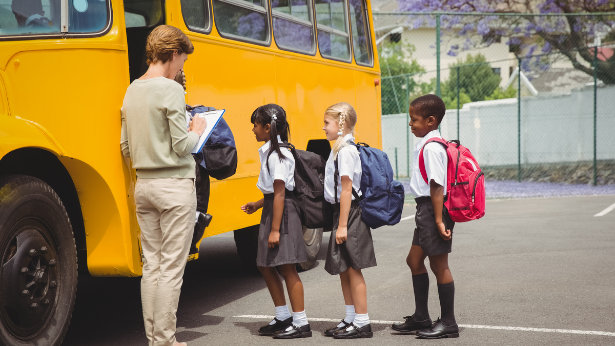 school kids boarding a bus with a female treacher