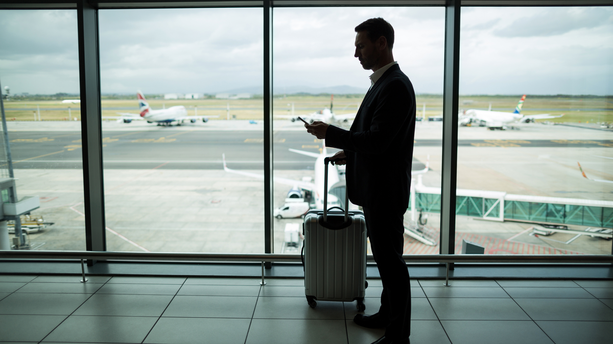 Man with a luggage standing on an airport lounge with the runway at the background.